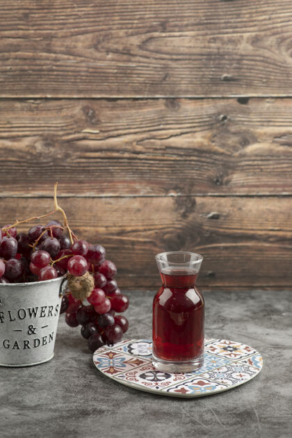 成熟大理石桌上放着一桶红色的新鲜葡萄和一杯果汁水果集群玻璃