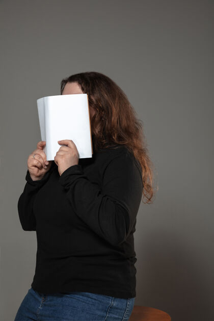 学习女人在灰色的墙上看书时用书遮住脸识字女人概念