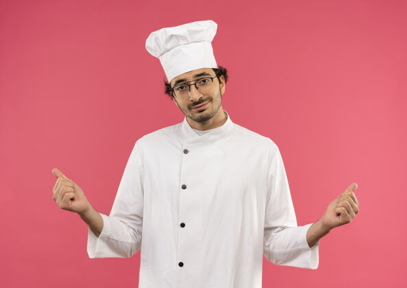 烹饪年轻的男厨师穿着厨师制服 戴着一副眼镜 在粉红色的墙上显示着“是”的手势眼镜制服穿着