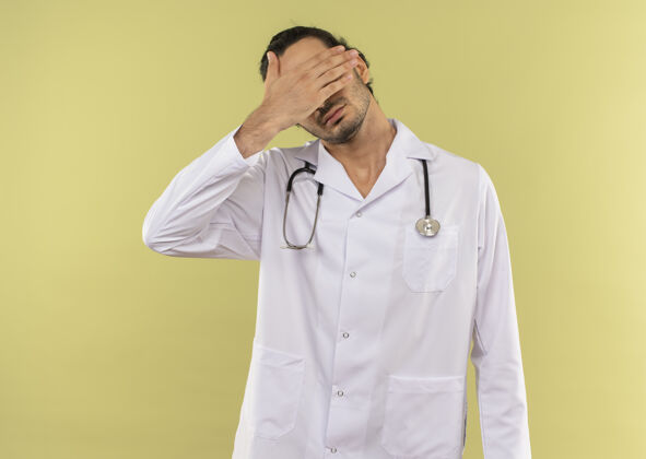 医生年轻的男医生戴着眼镜 穿着白色长袍 用听诊器捂着脸 手放在隔离的绿墙上 留着复印空间戴手脸