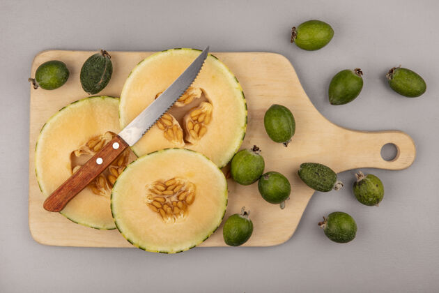 新鲜新鲜的哈密瓜片的俯视图 在灰色的墙壁上用刀将菲乔斯隔离在木制的厨房板上木头菲乔哈密瓜