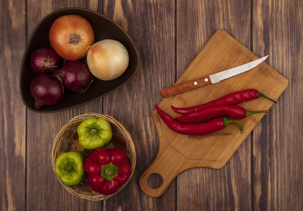 刀顶视图新鲜的辣椒在一个木制的厨房板与刀子洋葱在一个碗与甜椒桶在一个木制的墙壁铃铛烹饪自然