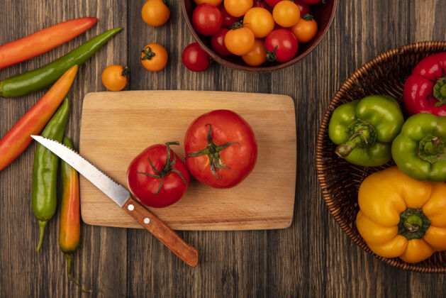 农业木制菜板上的美味红色大番茄俯视图 刀子上放着樱桃番茄 木碗上放着樱桃番茄 木桶上放着甜椒厨房顶部碗
