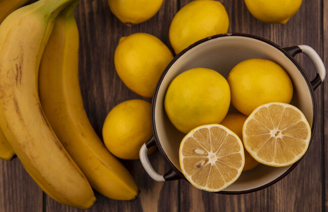 切片顶视图明亮的黄色半柠檬在一个碗柠檬和香蕉隔离在一个木墙上明亮木材顶部