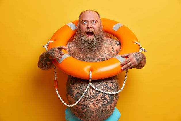 胡须怒气冲冲的大胡子胖子怒吼 直指 身上有纹身 摆着充气的救生圈 指点着怎么游泳 胃愤怒男人