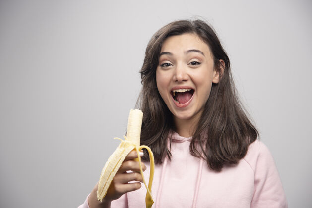 年轻年轻的女人在灰色的墙上吃香蕉女人水果女性