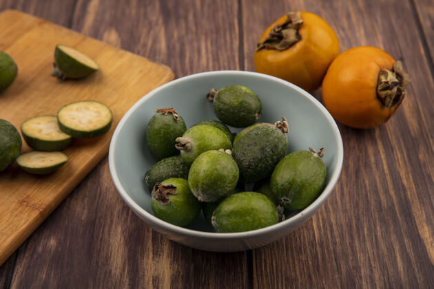 碗一个碗上的绿色蜜饯俯视图 木制厨房板上有蜜饯片 木制墙壁上有柿子水果切片柿子厨房