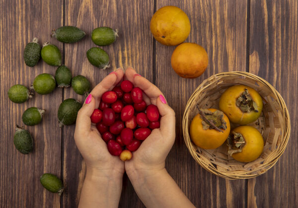 顶俯视图：女性手拿着新鲜的红凤梨和新鲜的柿子水果放在木桶上 把飞珠孤立在一堵墙上雌性柿子抱