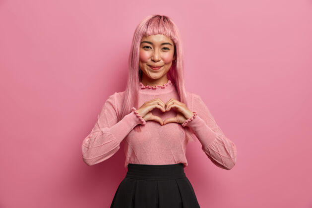 欢呼年轻浪漫的亚洲女人的肖像塑造了对爱人的心形 表达了爱意和爱意 表达了同情 戴着粉红色的长假发女人美丽浪漫
