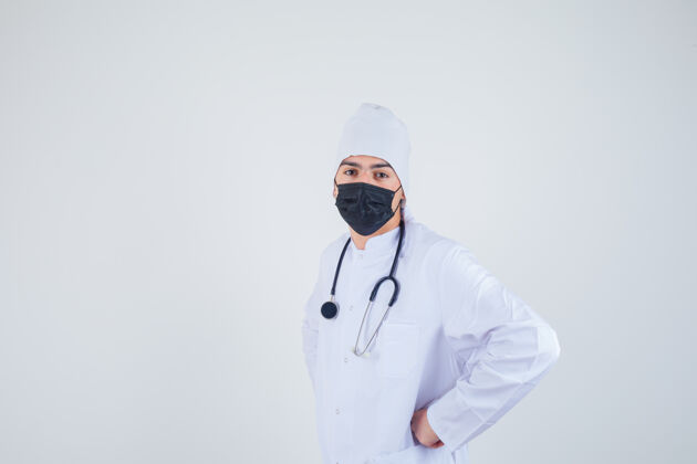 诊所年轻人手放在腰上 穿着白色制服 戴着面具 看上去很自信正面图微笑护理健康