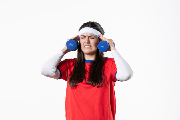 人正面图穿着运动服的年轻女性在白墙上用哑铃锻炼健身房球员运动