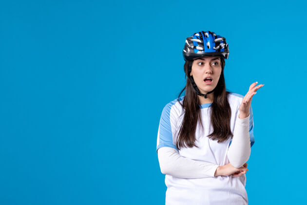 头盔前视图穿着运动服的年轻女性 蓝色墙上戴着头盔前面肖像惊喜