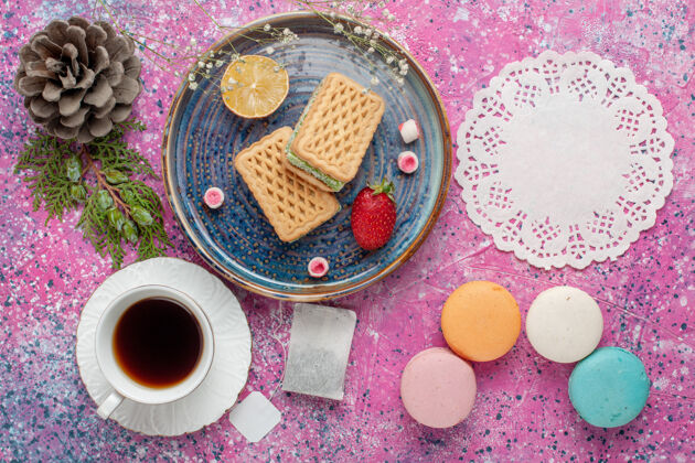 化妆品美味的华夫饼 美味的法国马卡龙和粉红色表面的茶的俯视图洗漱用品饼干华夫饼
