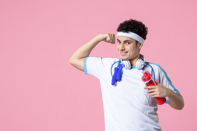 肖像正面图强壮的男性健身男子带着耳机和水瓶前面粉红男