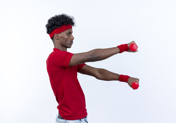 表情站在侧视图年轻的非裔美国人运动男子戴着头带和腕带举着哑铃在一边孤立的白色侧面腕带男人