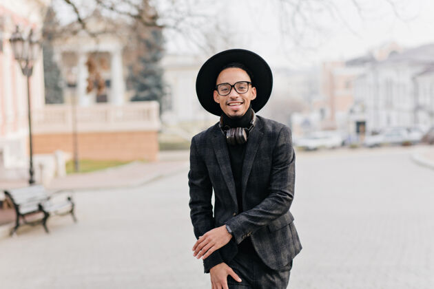 帽子早上 一个穿着深色西装戴着帽子的年轻人在公园里散步一张穿着时髦衣服的非洲男模微笑的户外照片放松城镇配饰