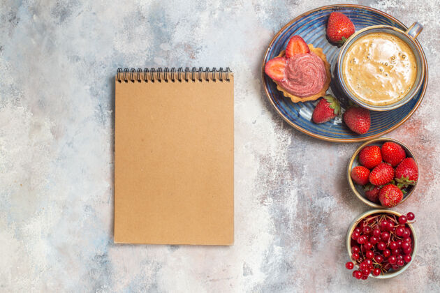 顶部顶视图一杯咖啡 蛋糕和红色水果放在浅色地板上 甜甜的饼干蛋糕笔记本蜡笔空白