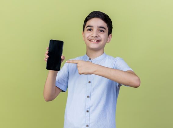 感觉微笑的小男孩指着手机 看着橄榄绿墙上孤立的前方脸年轻人表演
