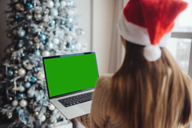 科技戴着圣诞老人的女人微笑着在笔记本电脑上和网友聊天在线笔记本电脑举行