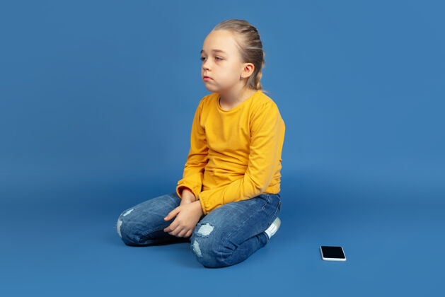 背景孤独地坐在蓝色背景上的悲伤小女孩的画像家庭孤独抑郁