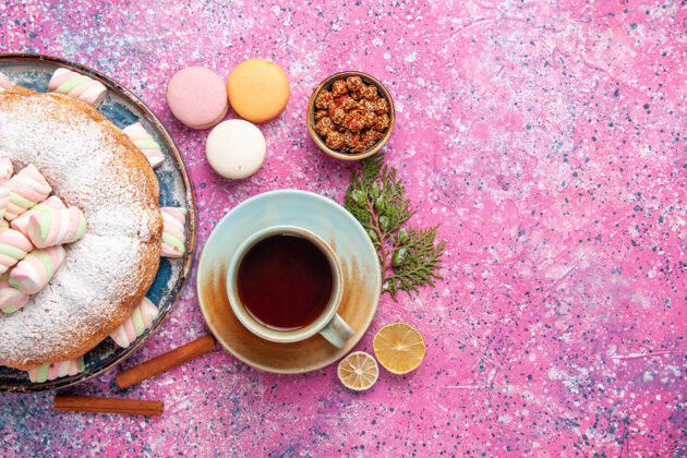 粉红色表面上的糖粉蛋糕 茶和法国马卡龙的俯视图早餐咖啡粉末