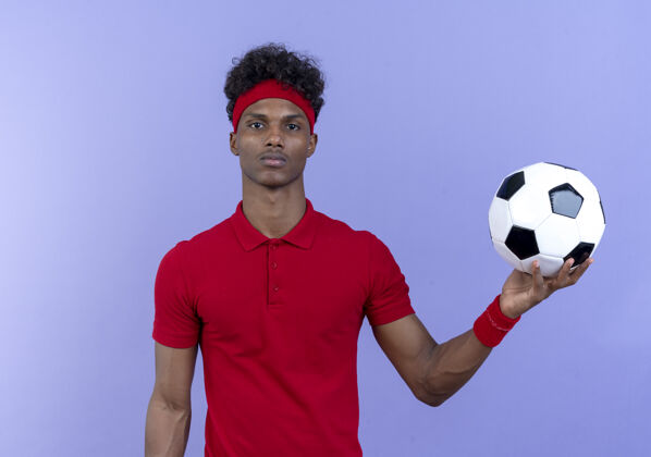 头带年轻的美国黑人运动男子戴着头带和腕带 把球举到隔离在蓝色墙上的一边穿壁板腕带