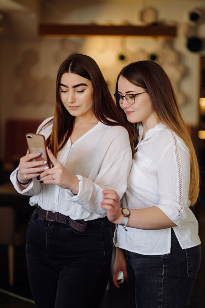 团体两个年轻女孩在咖啡馆用智能手机成人青年坐着