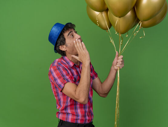 耳语印象深刻的中年党人站在侧视图举行气球看着他们耳语隔离在绿色墙上人黄金表情