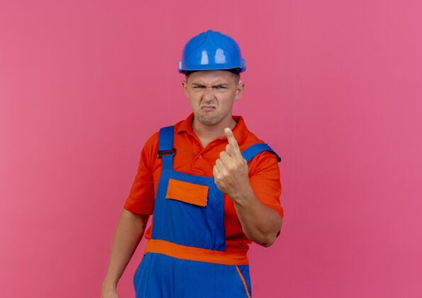 不愉快未出租的年轻男性建筑工人穿着制服和安全帽显示一个粉红色头盔建筑工人男性