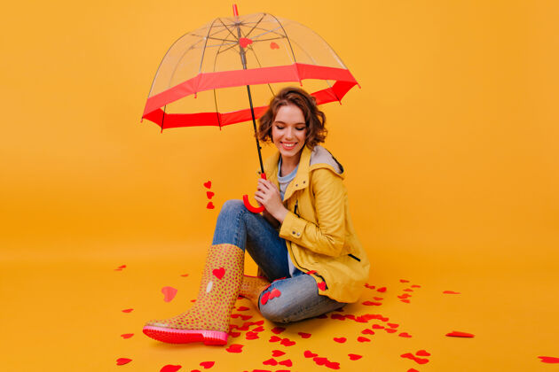 优雅幸福的女孩穿着胶鞋 打着伞坐在地上笑着快乐的白色女人穿着秋衣 享受着情人节季节青春肖像