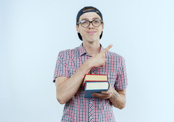 请高兴的年轻学生男孩背着书包 戴着眼镜 戴着帽子 手里拿着书 边上点着白色的空间背复制