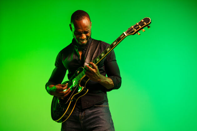 声音年轻的非洲裔美国音乐家 在渐变的绿黄色背景下像摇滚明星一样弹吉他背景旋律俱乐部