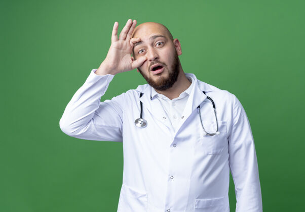 手惊讶的年轻男医生穿着医用长袍和听诊器睁开眼睛用手隔离在绿色男性医生听诊器