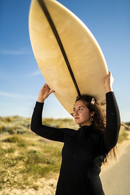 阳光一个迷人的女性头上举着冲浪板的垂直镜头模特娱乐健身