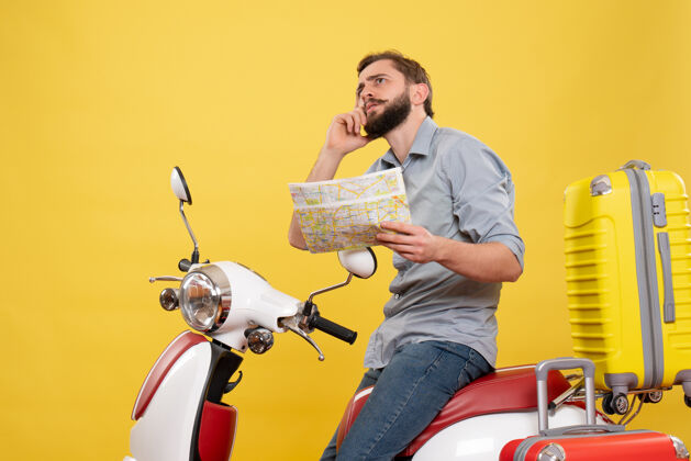 地图旅行的概念与思考的年轻人坐在摩托车上的手提箱 并持有黄色地图人手提箱持有