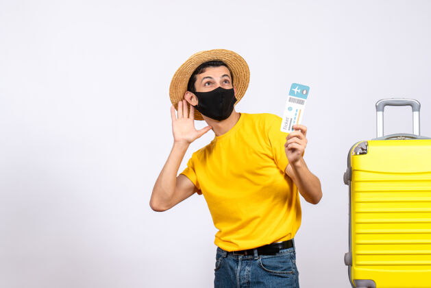 向上正面图身着黄色t恤的年轻人站在黄色手提箱旁 手里拿着旅行票抱着柱塞近