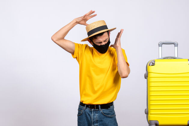 工作前视图穿着黄色t恤的愤怒的年轻人站在黄色手提箱旁边手提箱建筑微笑