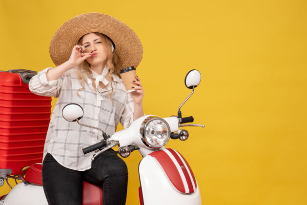人年轻女子戴着帽子 坐在摩托车上 拿着咖啡做出完美的姿势穿玩孩子