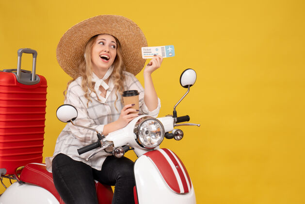 成人自信的年轻女子戴着帽子 坐在摩托车上 手里拿着咖啡和黄色的车票帽子摩托车年轻女子