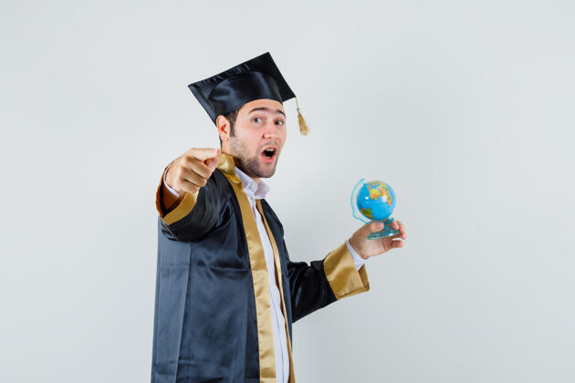 毕业年轻人拿着学校的地球仪 指着身着毕业制服的摄像机 正对着镜头朋友年轻指点