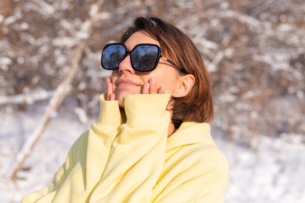 冬天阳光明媚的日子里 雪景冬林中一位年轻美女的画像 身着黄色大套头衫 戴着墨镜 享受着阳光和雪漂亮人娱乐