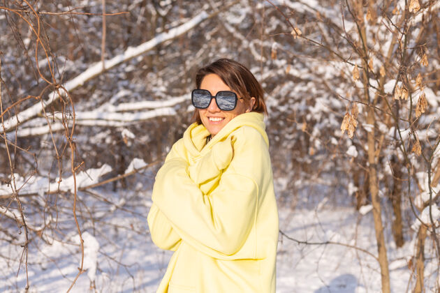 人阳光明媚的日子里 雪景冬林中一位年轻美女的画像 身着黄色大套头衫 戴着墨镜 享受着阳光和雪山太阳镜眼镜