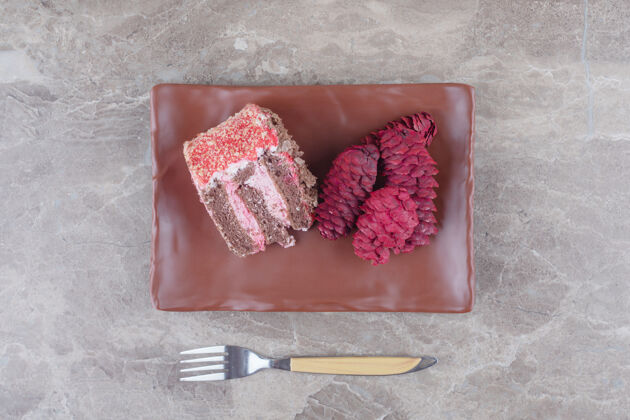 糕点一块蛋糕和红松球果放在一个盘子里 旁边是一个大理石叉子甜点蛋卷叉子