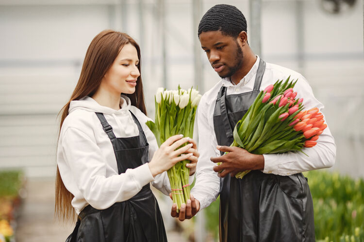 花店花束郁金香在一个男孩男孩和女孩在一个温室园丁在围裙工人微笑美丽