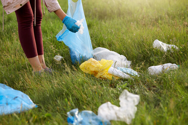 领域穿着紧身裤和手套的女志愿者在草地上捡垃圾 用蓝色垃圾袋社区责任女人