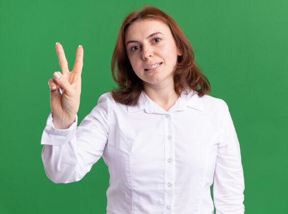年轻人穿白衬衫的年轻女子看着前面的展台 用手指指着绿色的墙指指点点秀出来手指