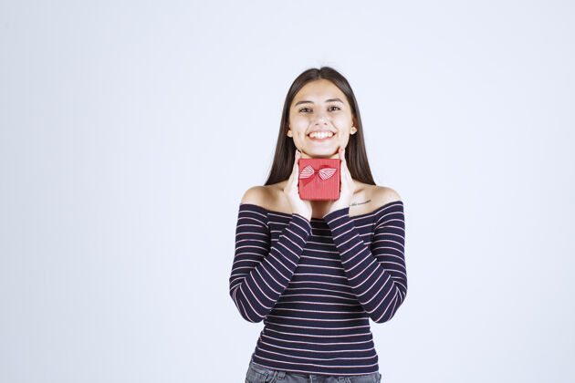 快乐穿着条纹衬衫的女孩拿着一个红色的礼盒 看起来很兴奋年轻人年轻刺激