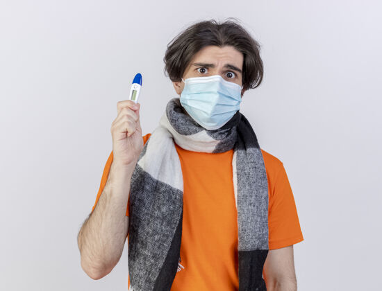 抱着困惑的年轻病人戴着围巾和医用面罩拿着温度计隔离在白色背景上医学迷糊年轻