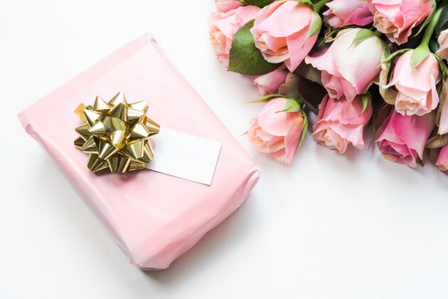 礼品用粉色纸包装的礼品盒 旁边有一束美丽的粉色玫瑰 上面有一条丝带礼品盒周年纪念情人节
