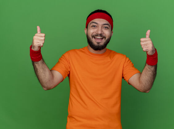 运动微笑的年轻人戴着头带和腕带 竖起大拇指 绿色背景下孤立的运动腕带拇指微笑
